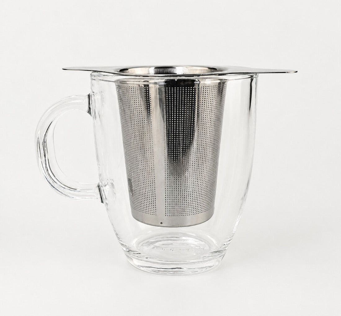 A winged stainless steel infuser basket resting on the rim of a clear glass mug