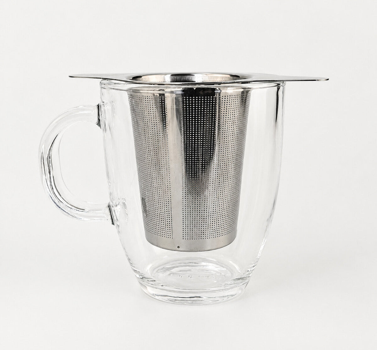 A winged stainless steel infuser basket resting on the rim of a clear glass mug