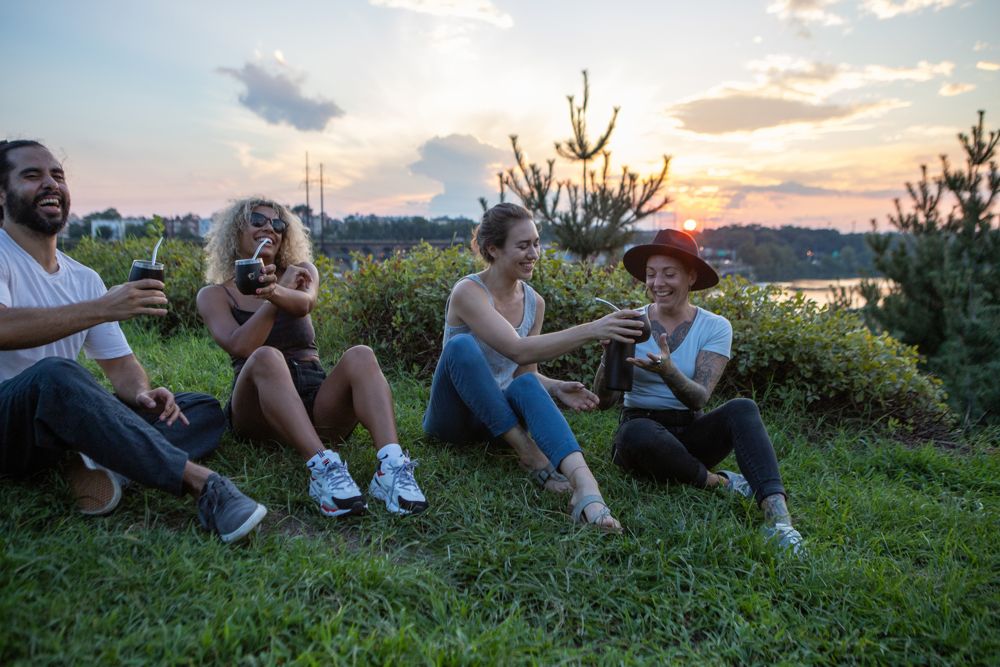 A group of four friends laugh together on a rocky hilltop sharing Yerba Crew mate at sunset.