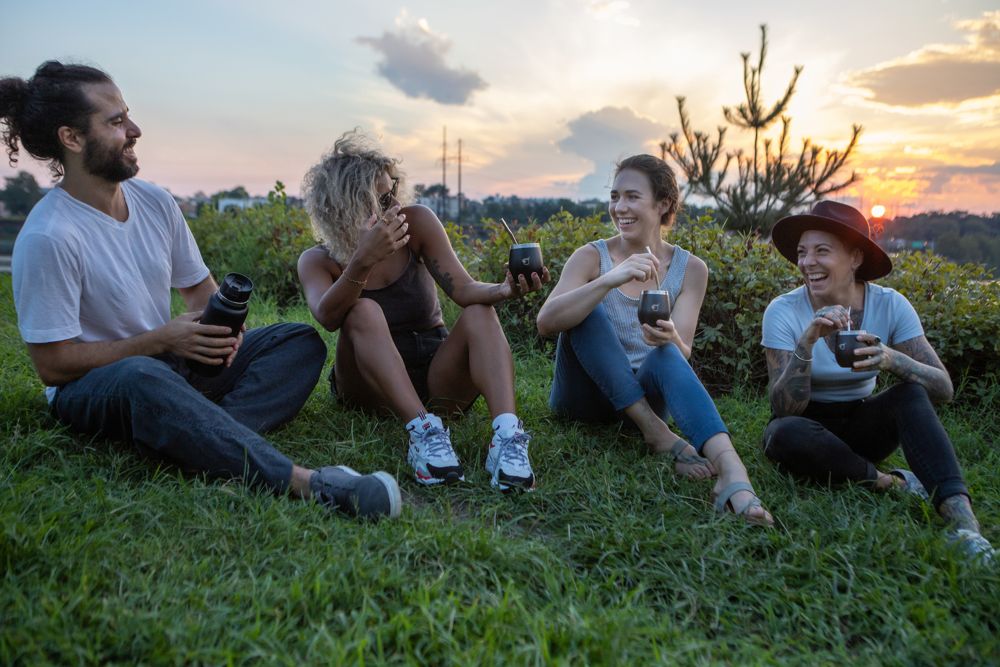 A group of four friends sit together on a rocky hilltop sharing Yerba Crew mate at sunset.