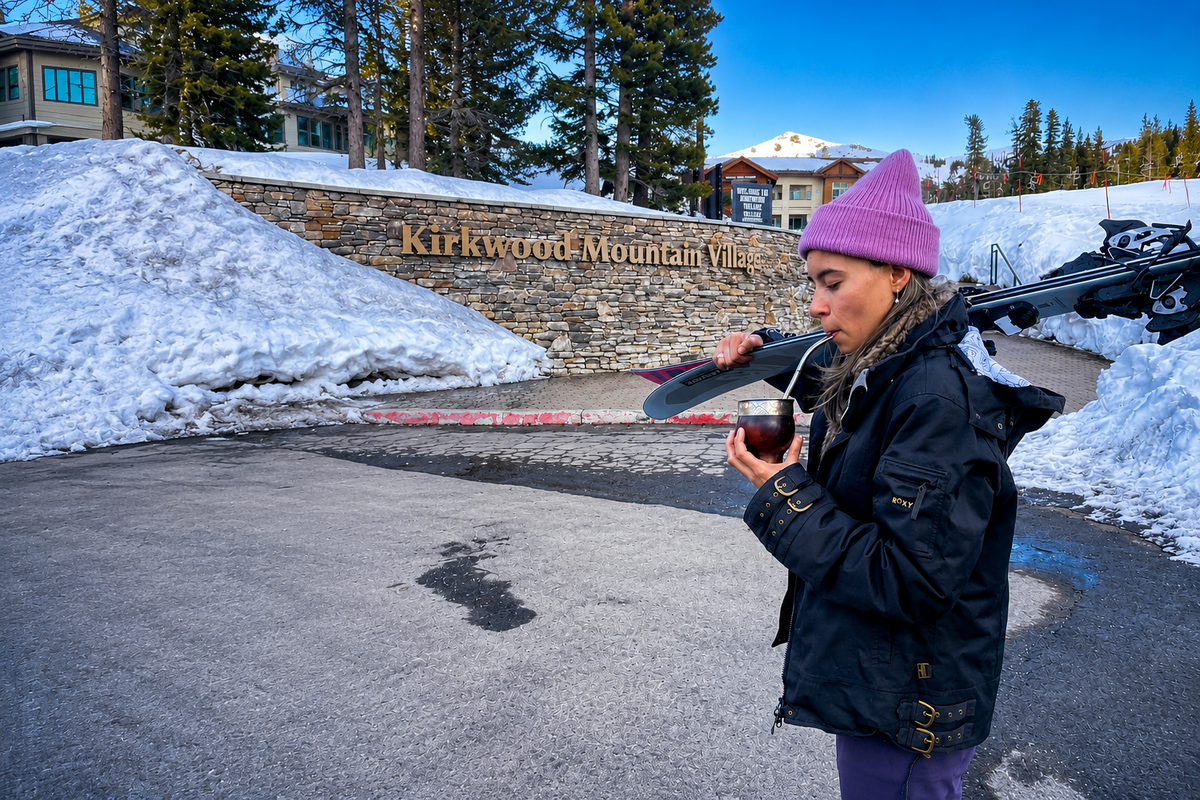 A woman in a pink beanie holds her skis and sips yerba mate through a bombilla at the entrance to Kirkwood Mountain Village.
