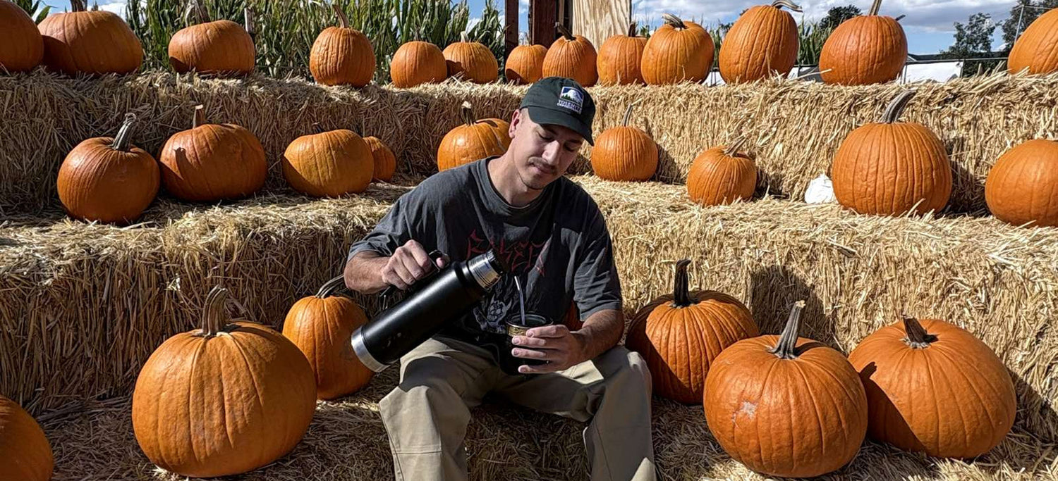 Person sitting on hay bales with pumpkins in the background drinking yerba mate