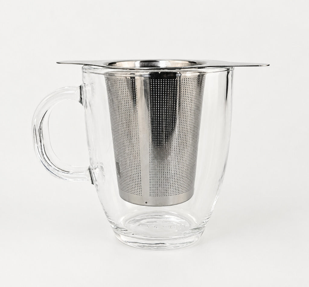 A winged stainless steel infuser basket resting on the rim of a clear glass mug.
