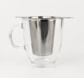 A winged stainless steel infuser basket resting on the rim of a clear glass mug.