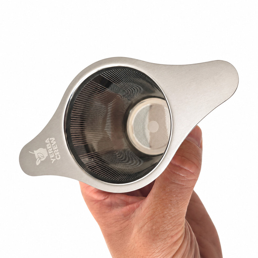 Top-down view of the winged infuser basket held in a hand, showing the leaf logo on the flat wing.