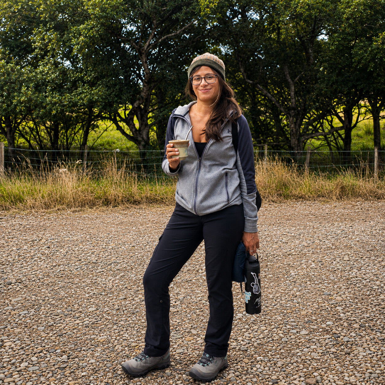 A woman drinking yerba mate from the Iruya ceramic gourd while walking on a gravel path in the countryside.
